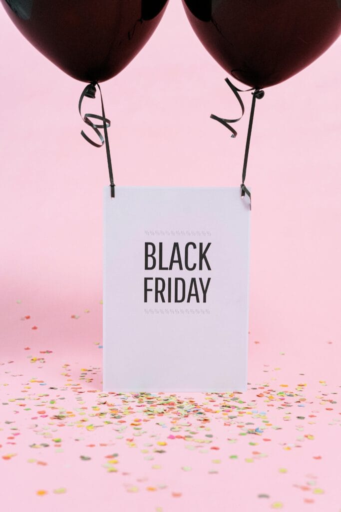 Black Friday promotion with black balloons and confetti on pink background.